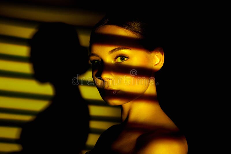 Sunset light falling through the blinds on the face of beautiful girl