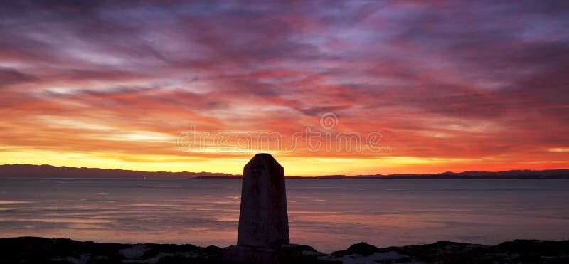 A colorful, dramatic sunset from San Juan island looking west towards the Straits of Juan de Fuca and Vancouver Island. The concrete obelisk in the foreground is a US geological marker. A colorful, dramatic sunset from San Juan island looking west towards the Straits of Juan de Fuca and Vancouver Island. The concrete obelisk in the foreground is a US geological marker.