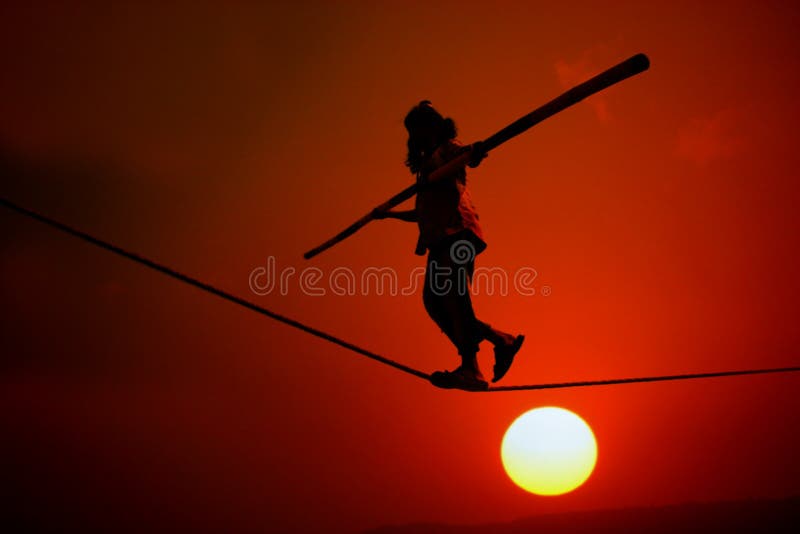 A silhouette of a poor girl working doing trapeze acts like walking on a rope on the side of a street at sunset. A silhouette of a poor girl working doing trapeze acts like walking on a rope on the side of a street at sunset.