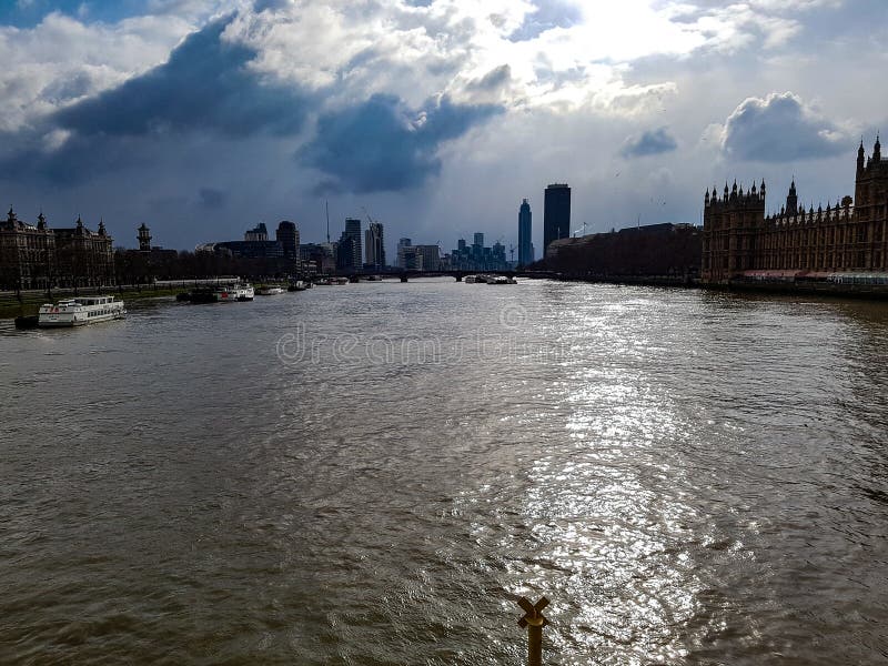 Sunshine through big clouds to river Thames in London view from bridge to London city skyscraper westminster abbey boats, uk britain.