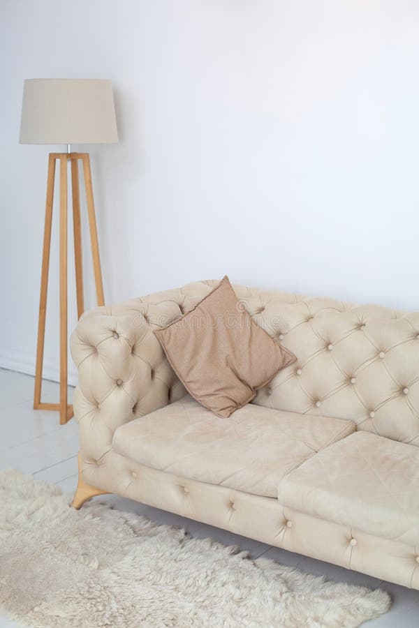 Suolo beige con cuscino decorativo e lampada in un spazioso soggiorno bianco Stanza interna con divano confortevole su parete bia fotografia stock
