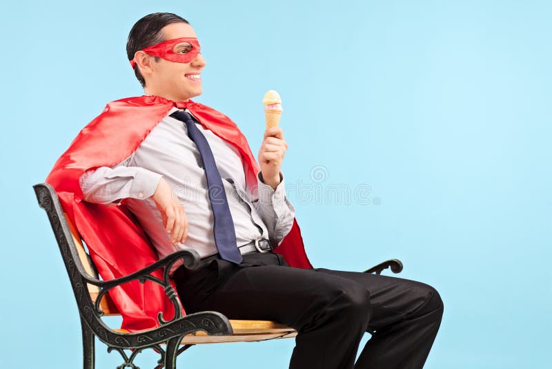 Super héroe que sostiene un helado asentado en banco foto de archivo Super héroe que sostiene un helado asentado en banco foto de archivo