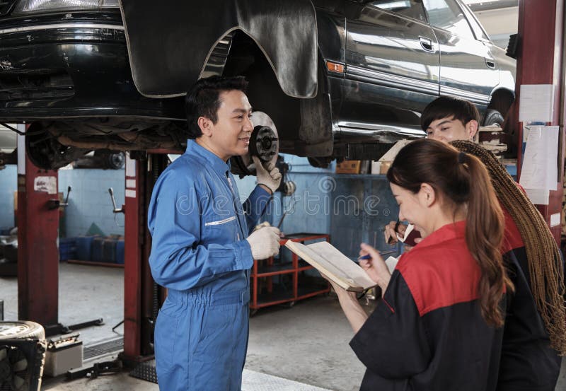 Asian male professional automotive engineer supervisor describes car wheel and suspension repair work with mechanic worker staffs team in fix service garage, specialist occupations in auto industry. Asian male professional automotive engineer supervisor describes car wheel and suspension repair work with mechanic worker staffs team in fix service garage, specialist occupations in auto industry.