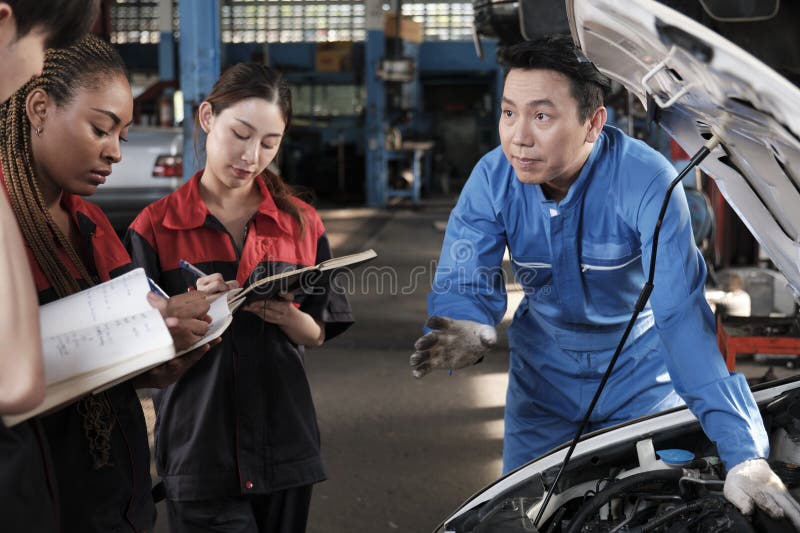 Asian male professional automotive engineer supervisor describes car engine maintenance and repair work with mechanic worker staffs team in fix service garage, specialist occupations in auto industry. Asian male professional automotive engineer supervisor describes car engine maintenance and repair work with mechanic worker staffs team in fix service garage, specialist occupations in auto industry.