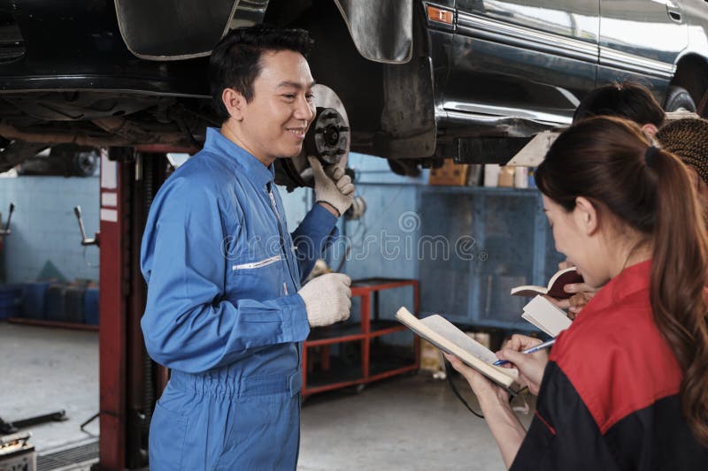 Asian male professional automotive engineer supervisor describes car wheel and suspension repair work with mechanic worker staffs team in fix service garage, specialist occupations in auto industry. Asian male professional automotive engineer supervisor describes car wheel and suspension repair work with mechanic worker staffs team in fix service garage, specialist occupations in auto industry.