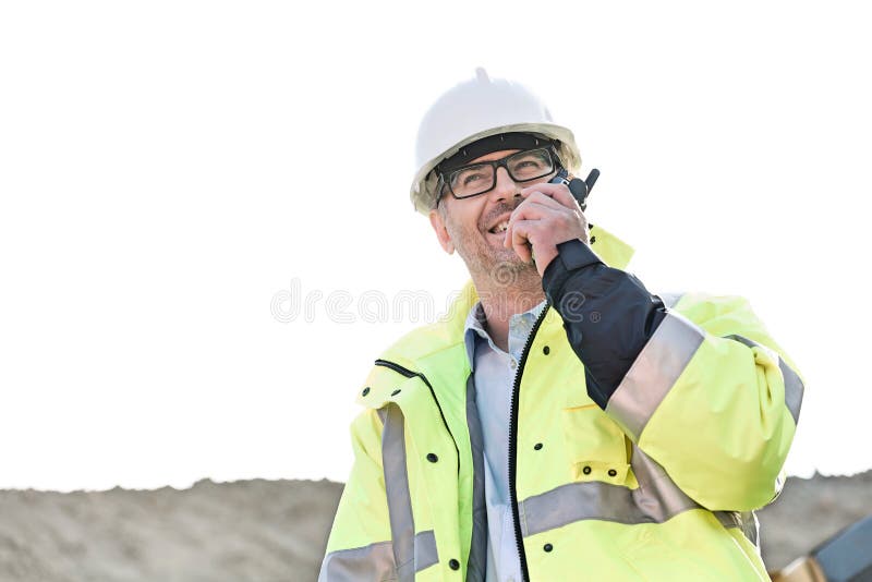 Supervizor fericit care utilizează walkietalkie la locul de construcție împotriva cerului senin royalty free stock images