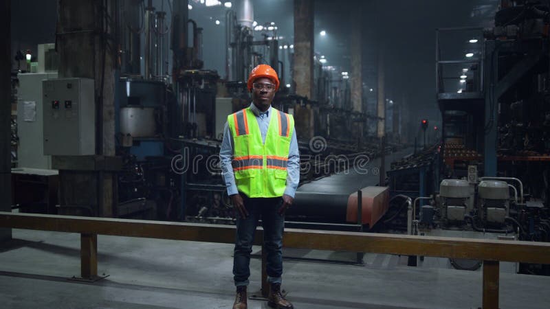 Supervizor fericit purtând o uniformă de siguranță în facilitatea modernă. Inginer industrial la fabrică. un mecanic vesel cu păr negru care se uită la o cameră specială.
