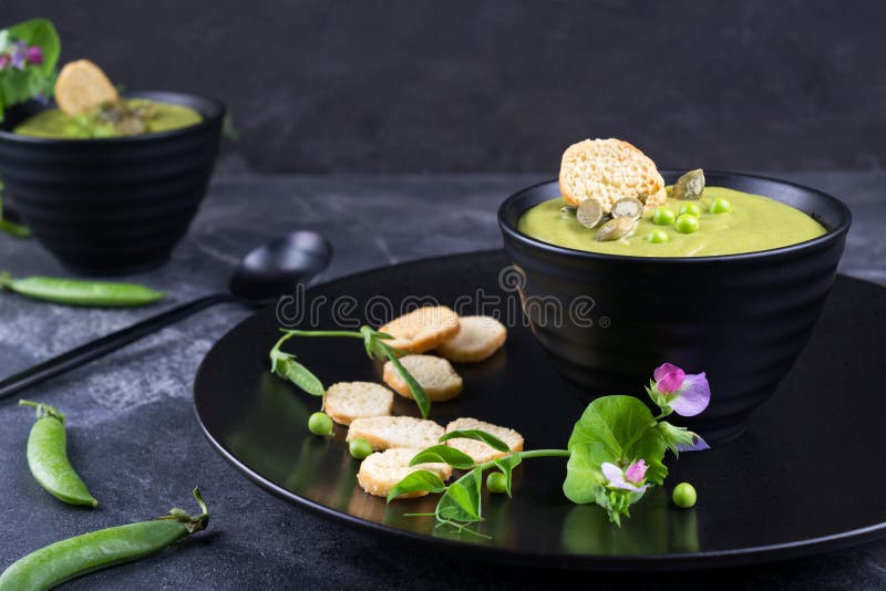 Suppenpüree der grünen Erbse mit Croutons in der schwarzen Schüssel Auf dunklem Stein stockfotografie Suppenpüree der grünen Erbse mit Croutons in der schwarzen Schüssel Auf dunklem Stein stockfotografie
