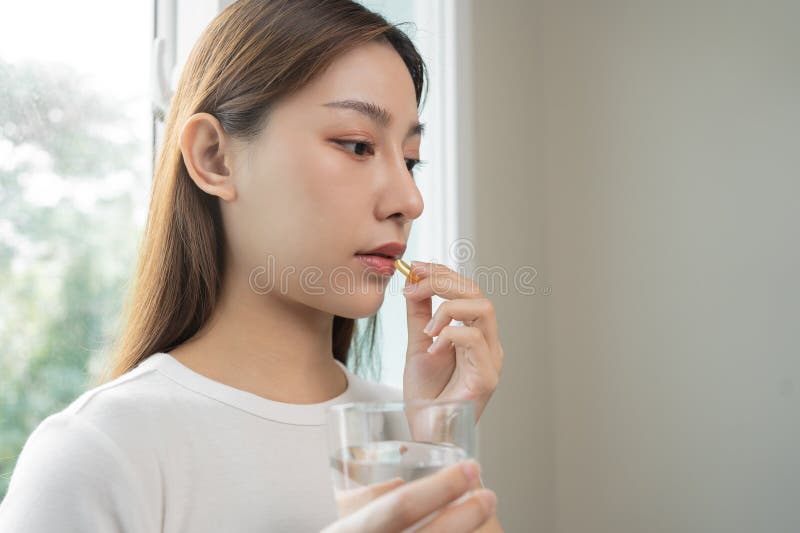 Supplemento dietetico, giovane donna asiatica, con mano in mano una pastiglia o una pillola gialla, prendere olio di pesce o vitam