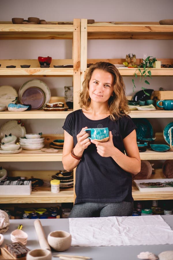 Support femelle avec les ustensiles de finition, lieu de travail de sourire de ceramist avec les tasses cuites au four image stock Support femelle avec les ustensiles de finition, lieu de travail de sourire de ceramist avec les tasses cuites au four image stock