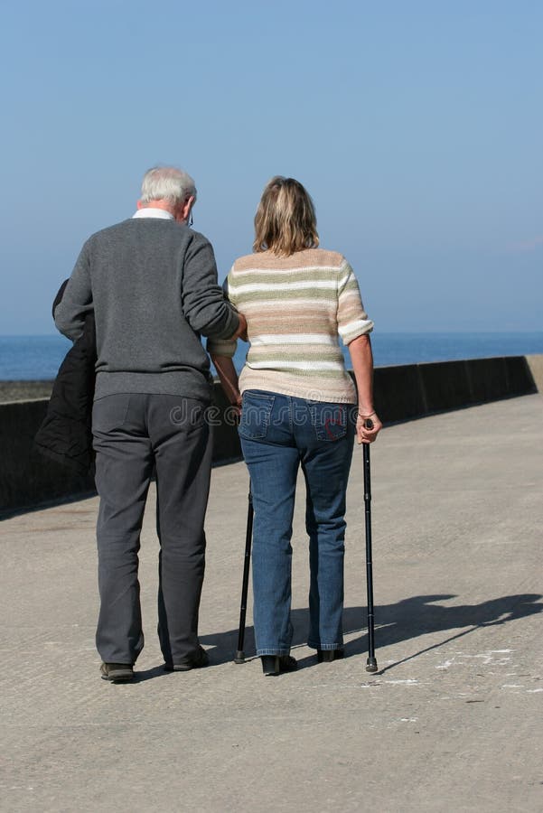 Más viejo hombre ayúdamos medio viejo una mujer sobre el caminando palos, cielo azul sobre el trasero.