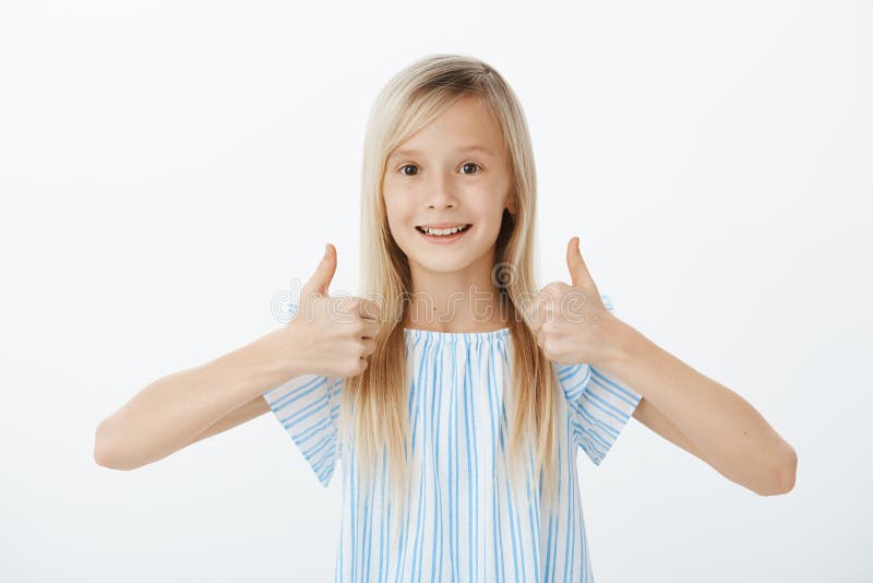 Supportive little friend wants to cheer mates. Happy positive cute girl with blond hair, raising thumbs up and giving stock photo Supportive little friend wants to cheer mates. Happy positive cute girl with blond hair, raising thumbs up and giving stock photo