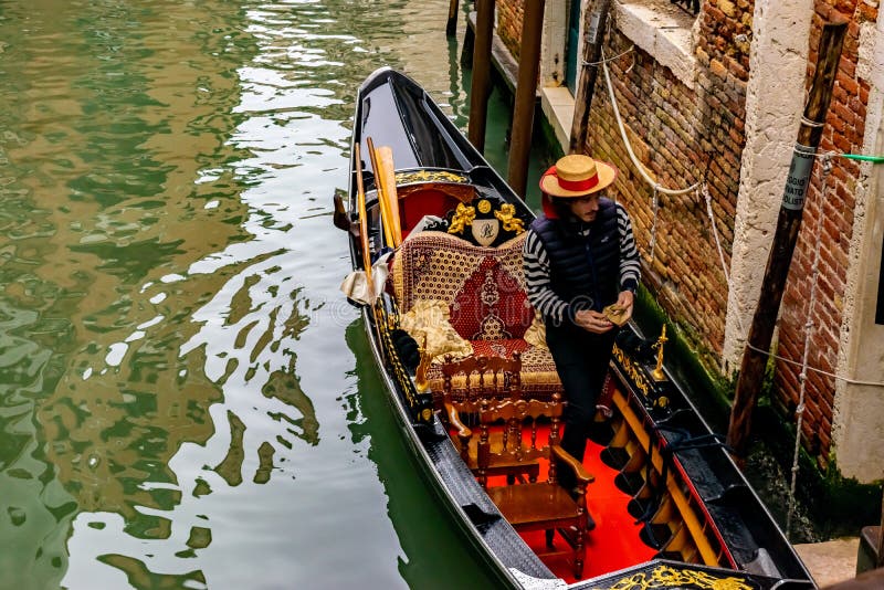 Supports de port de chapeau de paille de jeune gondolier italien attirant dans la gondole traditionnelle avec le d?cor de luxe photos libres de droits Supports de port de chapeau de paille de jeune gondolier italien attirant dans la gondole traditionnelle avec le d?cor de luxe photos libres de droits