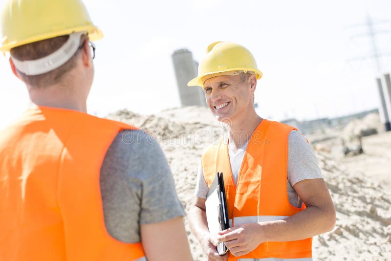 Supraveghetor fericit discutând cu colegul la locul de construcție stock image