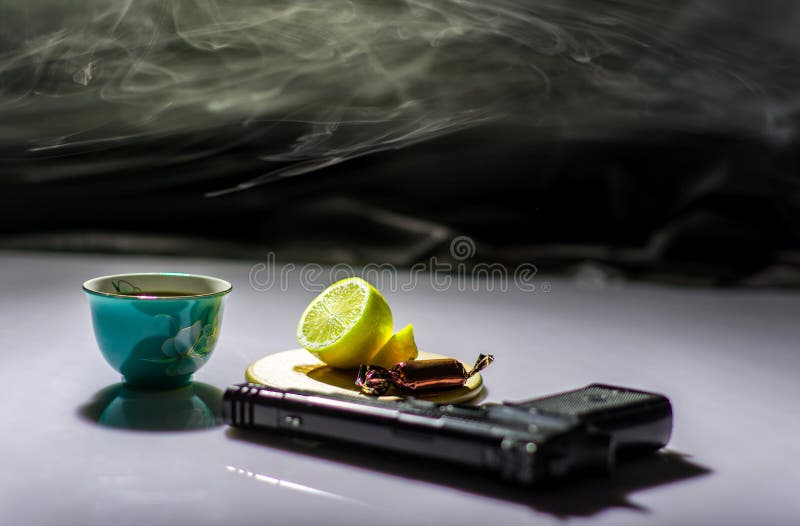 Sur la table une arme à feu et un thé avec le citron image stock Sur la table une arme à feu et un thé avec le citron image stock