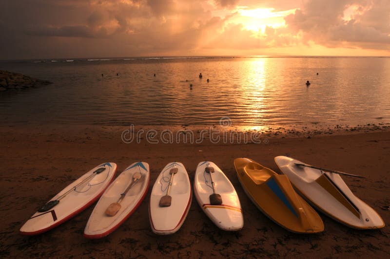 Surf boards line the beach decorating the rising sun on the coast of Sanur