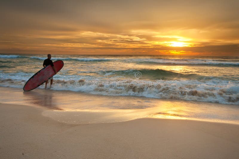 Surfer entrant dans l'océan au lever de soleil photographie stock