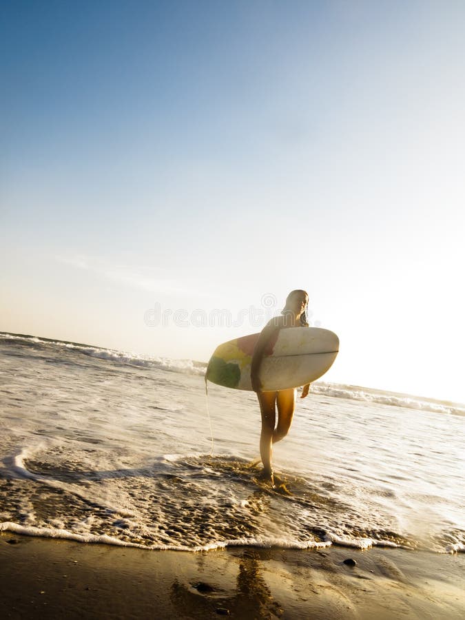 Surfer féminin avec le panneau de vague déferlante marchant sur la plage images stock Surfer féminin avec le panneau de vague déferlante marchant sur la plage images stock