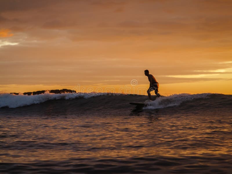 Surfer riding wave at Magnific Rock, Nicaragua at sunset