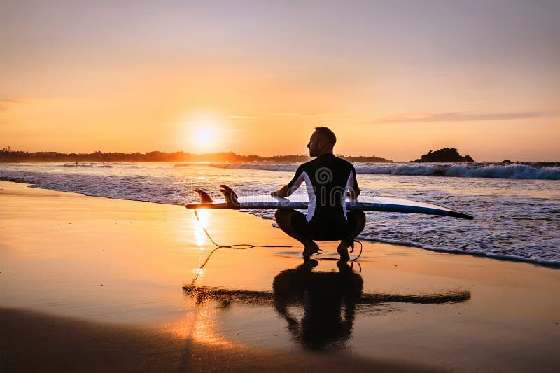 Surfer with Surfboard Sits on Ocean Surf Line at Sunset Time Stock