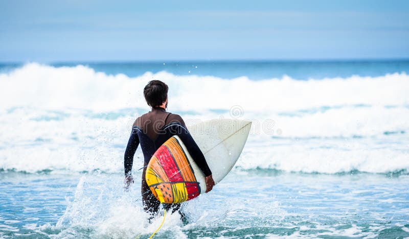 Surferkerel met surfplank het in hand lopen naar grote golven royalty-vrije stock afbeelding Surferkerel met surfplank het in hand lopen naar grote golven royalty-vrije stock afbeelding