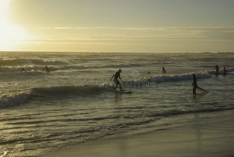 Surfers having surf lessons riding down small waves in sunset on beach near the city of gijon in spain. Surfers having surf lessons riding down small waves in sunset on beach near the city of gijon in spain