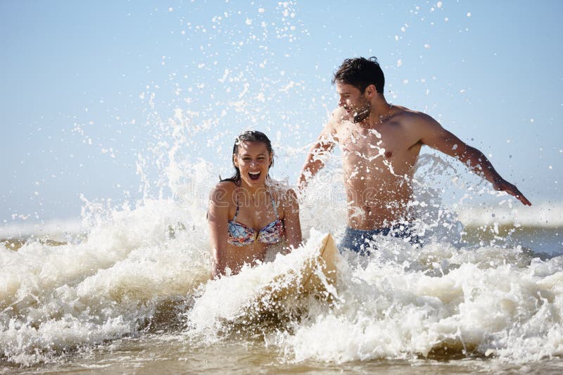 Surfing para i śmiech na plaży z falami pluskowymi i letnim łączeniem w oceanie. Hobby i morze obrazy stock