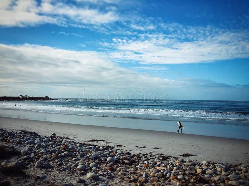 Surfer walking on beach with surf board. California, USA, pacific ocean coast. Blue cloudy sly in background. Surfer walking on beach with surf board. California, USA, pacific ocean coast. Blue cloudy sly in background.