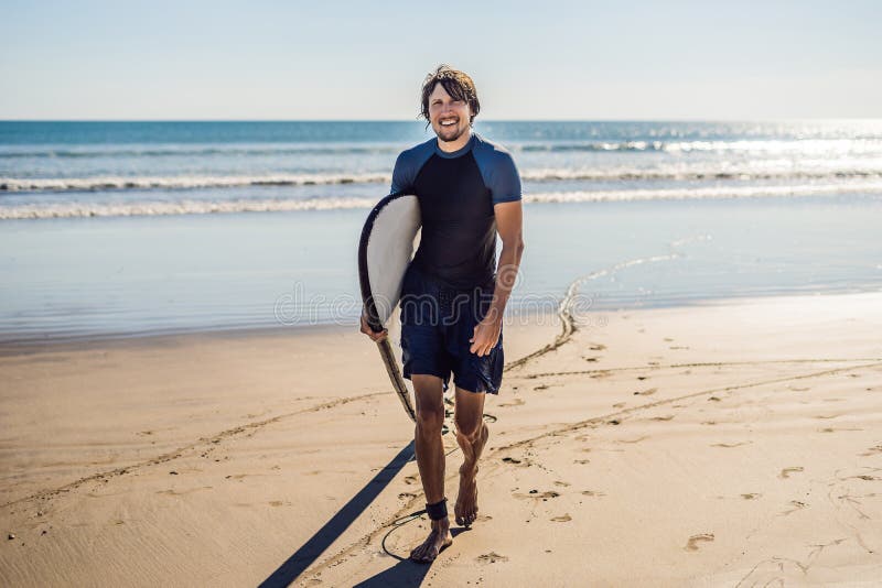 Surfista novo desportivo considerável que levanta com sua prancha sob o seu fotografia de stock Surfista novo desportivo considerável que levanta com sua prancha sob o seu fotografia de stock