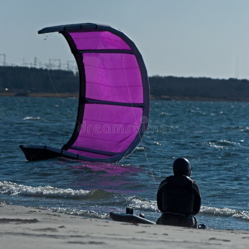 A nice and wet day with these safe kites surfers, in this blue sea at Swedens cold coast in april.....a surfer sitting on the beach and resting. A nice and wet day with these safe kites surfers, in this blue sea at Swedens cold coast in april.....a surfer sitting on the beach and resting