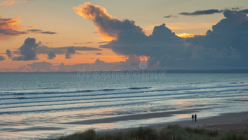 Surfisti che camminano avanti e che perfino spiaggia con un tramonto dietro loro immagine stock libera da diritti Surfisti che camminano avanti e che perfino spiaggia con un tramonto dietro loro immagine stock libera da diritti