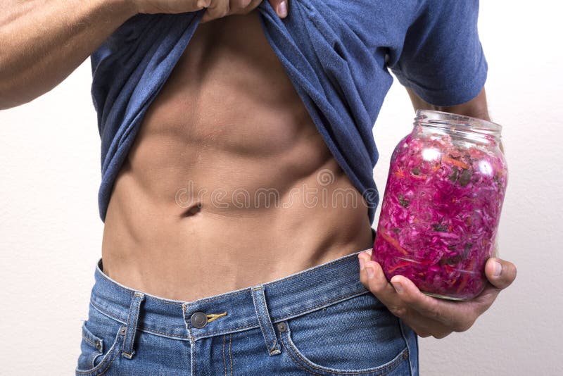 Closeup of man's abdominal muscles as he lifts shirt up while holding jar of red sauerkraut next to lean waist. Closeup of man's abdominal muscles as he lifts shirt up while holding jar of red sauerkraut next to lean waist