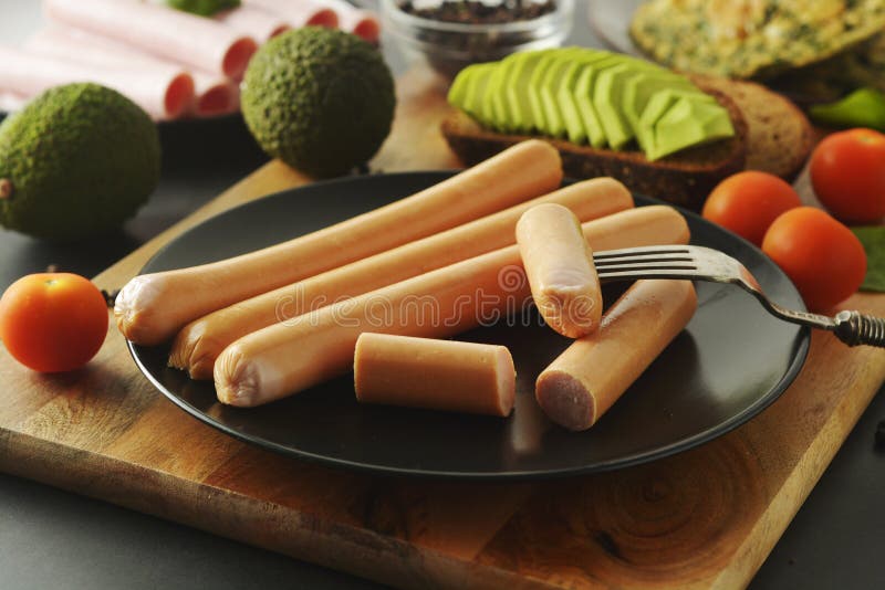 Surowego kurczaka hot dog mięsne kiełbasy śniadaniowe z avocado i pomidorami By? mo?e Kiełbasy w czarnym talerzu zdjęcie stock Surowego kurczaka hot dog mięsne kiełbasy śniadaniowe z avocado i pomidorami By? mo?e Kiełbasy w czarnym talerzu zdjęcie stock