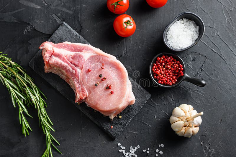 Surowy stek wieprzowy i pieprz solny na czarnej płycie z łupku z rozmarynu i świeżych składników do grillowania na czarno obraz royalty free