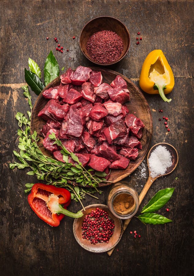 Surowy uncooked mięso pokrajać w sześcianach z świeżymi ziele, warzywami i pikantność na nieociosanym drewnianym tle, składniki d zdjęcia stock Surowy uncooked mięso pokrajać w sześcianach z świeżymi ziele, warzywami i pikantność na nieociosanym drewnianym tle, składniki d zdjęcia stock