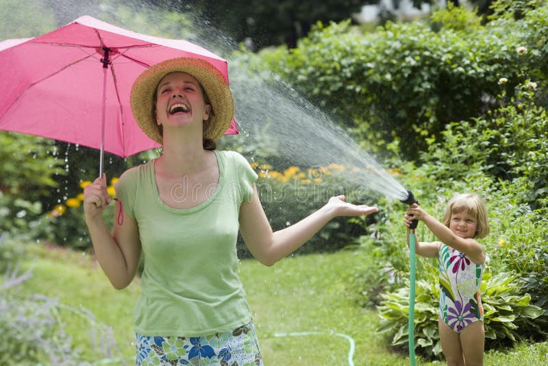 Little girl spraying woman with water from a garden hose in the Summertime. Little girl spraying woman with water from a garden hose in the Summertime