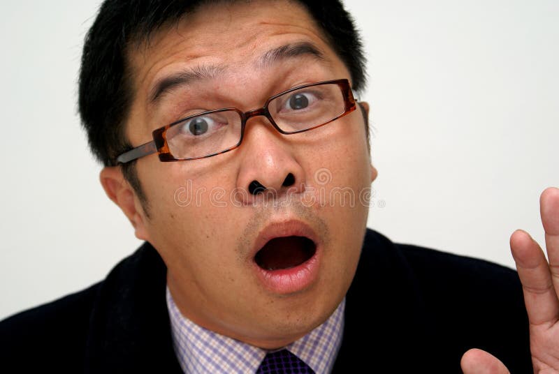 A surprised expression on an asian businessman of chinese descent. Wearing squarish spectacles, business attire and dark coat. Hand is upraised , open mouth and wide eyes. A surprised expression on an asian businessman of chinese descent. Wearing squarish spectacles, business attire and dark coat. Hand is upraised , open mouth and wide eyes.