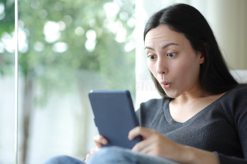 Surprised asian woman reading ebook reading at home royalty free stock image