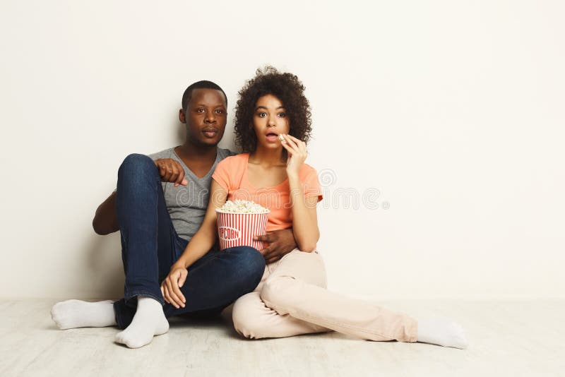 Surprised black couple wathing movie at home on the floor