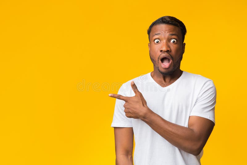 Surprised Black Man Pointing Finger Aside Standing In Studio.