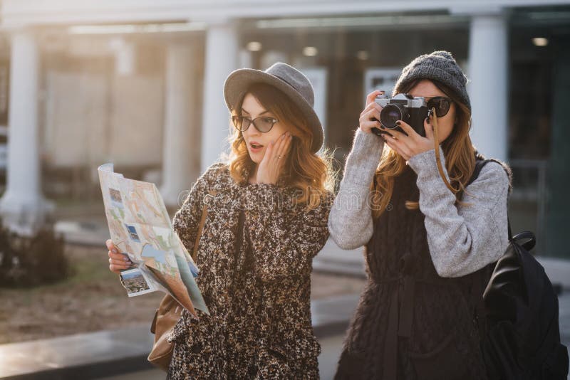 Surprised curly woman in glasses looking at map, touching face while her friend making photo of sights. Attractive stock images Surprised curly woman in glasses looking at map, touching face while her friend making photo of sights. Attractive stock images
