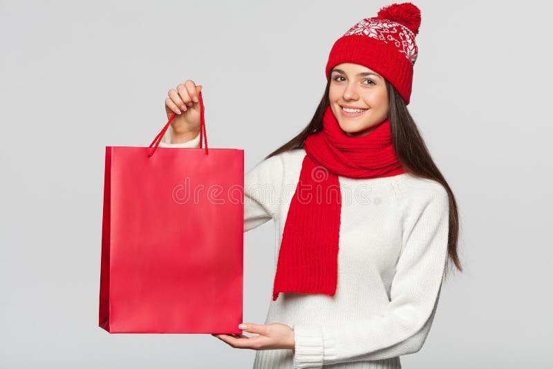 Surprised happy woman holding red bag in excitement, shopping. Christmas girl on winter sale with gift, isolated on gray