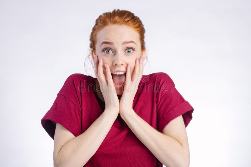 Surprised redhead young woman in red shirt wide open mouth and touching her head over white background. Surprised redhead young woman in red shirt wide open mouth and touching her head over white background