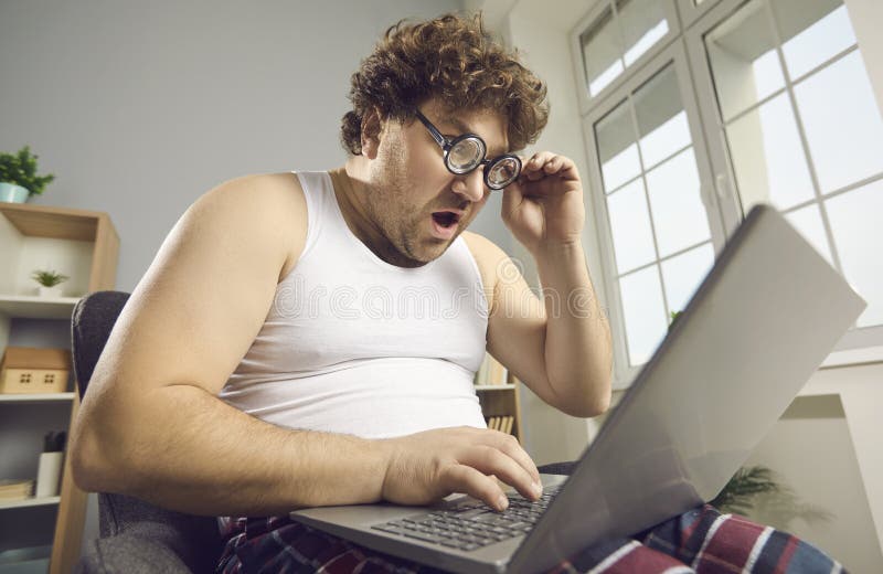 Surprised shocked funny fat man in pajamas reads amazing news on laptop. 