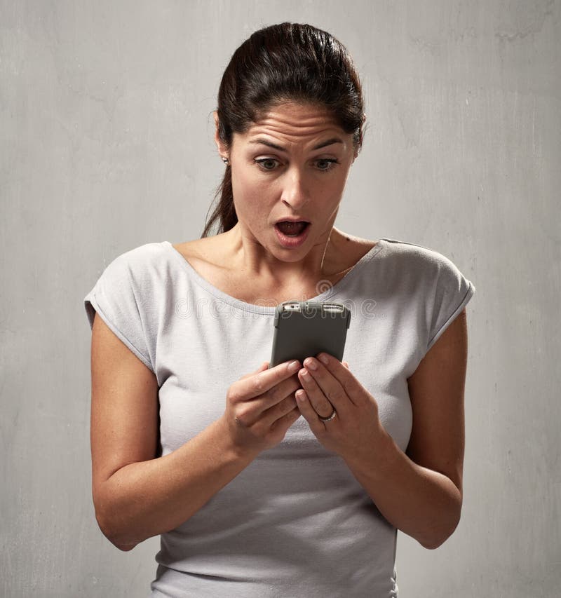 Surprised dissatisfied young woman with smartphone gray background. Surprised dissatisfied young woman with smartphone gray background