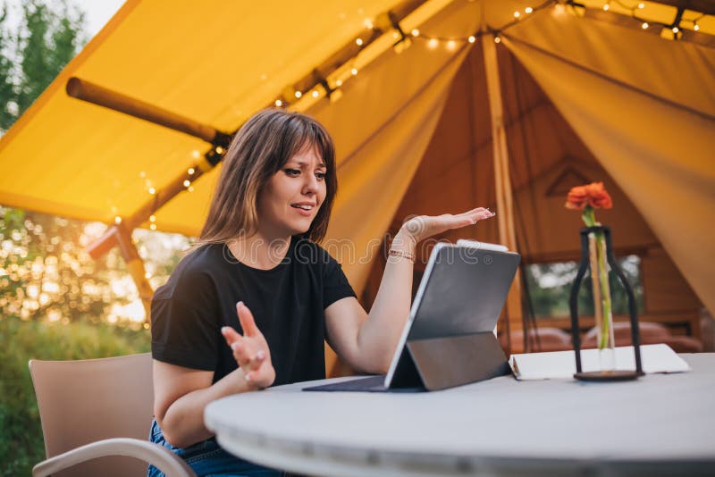 Surprised Woman freelancer using a laptop on a cozy glamping tent in a sunny day. Luxury camping tent for outdoor summer holiday