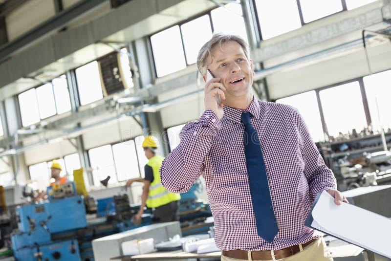 Surveillant masculin mûr avec le presse-papiers parlant au téléphone portable dans l'industrie photographie stock libre de droits Surveillant masculin mûr avec le presse-papiers parlant au téléphone portable dans l'industrie photographie stock libre de droits
