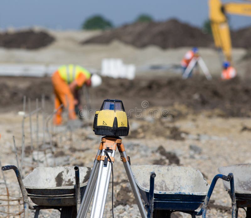 Rotating laser surveying equipment at road construction site with workers and dredger in background. Rotating laser surveying equipment at road construction site with workers and dredger in background