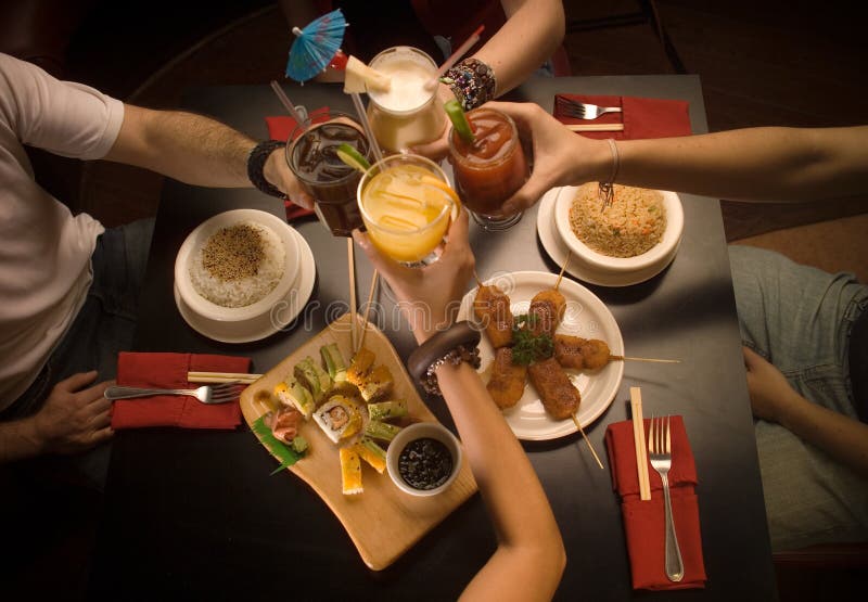 Quattro Persone celebrano evento brindando con i loro drink in un tavolo pieno di cibo sushi.