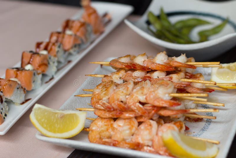 Sushi på en tabell Räkor, tigerrullar och edamame på vit plat arkivfoton Sushi på en tabell Räkor, tigerrullar och edamame på vit plat arkivfoton